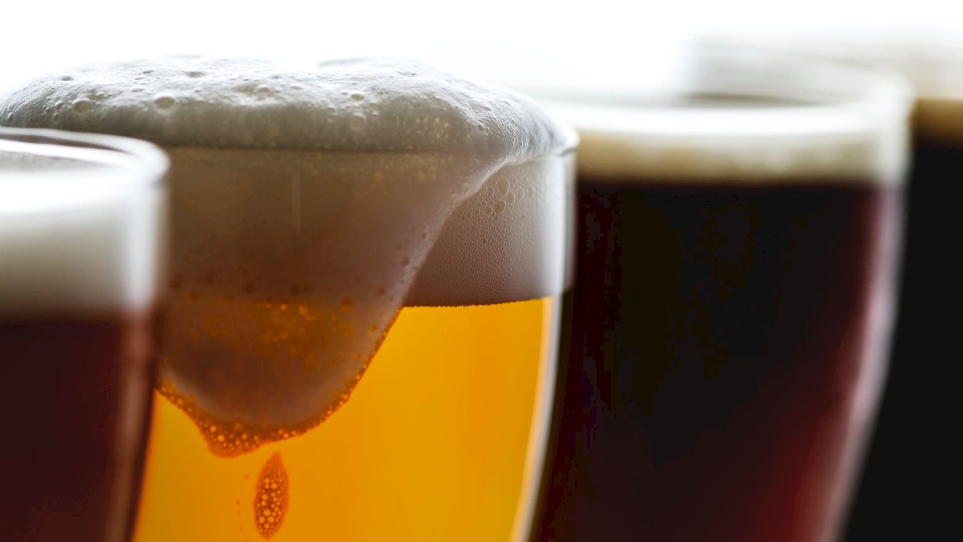 The image shows three glasses of beer, each with varying colors and levels of foam on top.