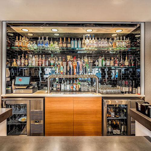 A well-stocked bar with various liquor bottles, beer taps, and a point-of-sale system; the bar's countertop and setup are visible.