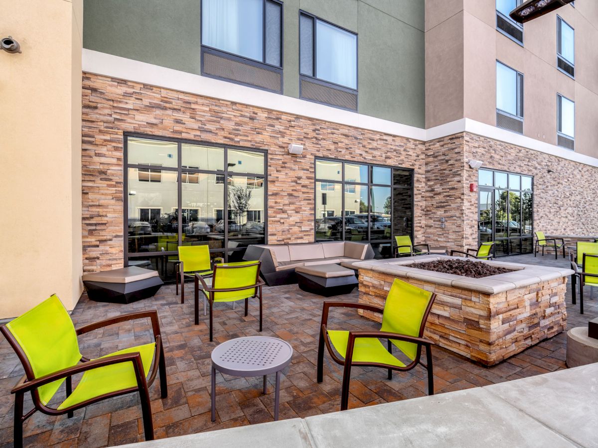 The image shows an outdoor patio area with green chairs, a fire pit, and a building in the background with large windows.