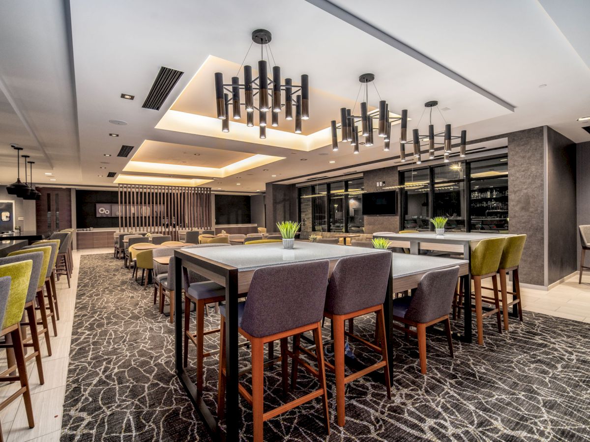 A modern, well-lit dining area with high ceilings, contemporary lighting fixtures, and a mix of high tables and chairs.