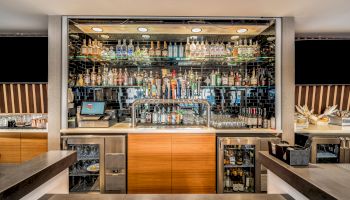 The image shows a well-organized bar with a variety of liquor bottles, a cash register, taps for draft beer, and bar tools on the counter.