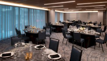 A beautifully set banquet hall with round tables, dark-themed chairs, folded napkins, and elegant table settings ready for a formal event or gathering.