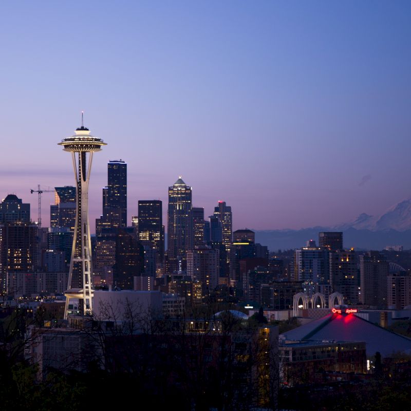 The image shows the Seattle skyline at dusk, featuring the Space Needle, downtown skyscrapers, and Mount Rainier in the background.