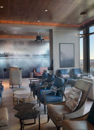 A modern lounge with comfortable seating, a mural of a city skyline, and large windows offering a scenic view of the bay and a Ferris wheel.