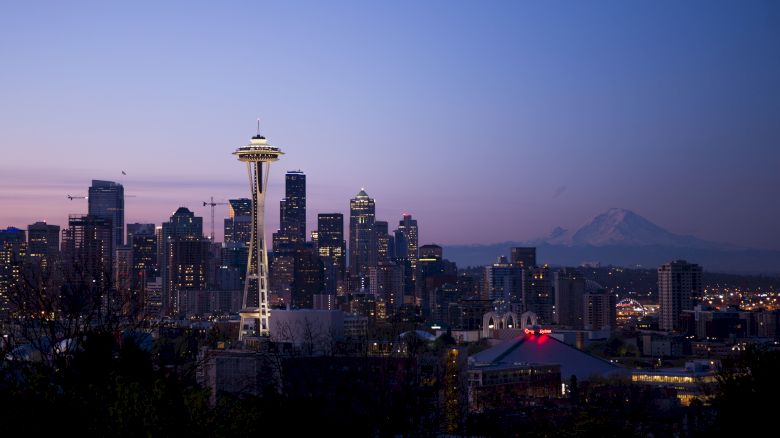 The image shows the Seattle skyline at twilight, with the Space Needle prominently featured and Mount Rainier in the background.
