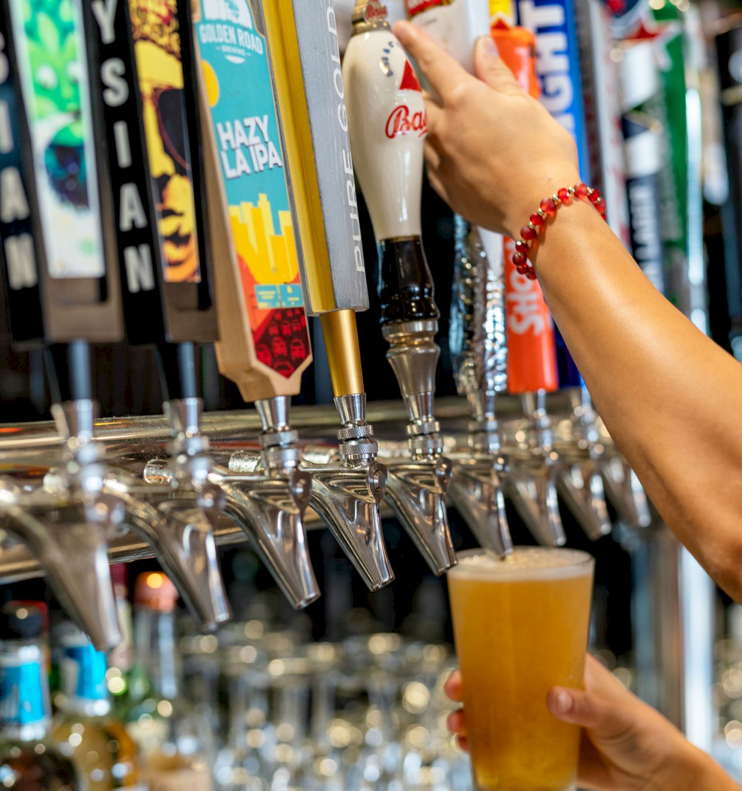 A person is pouring beer from a tap at a bar, with multiple taps and different beer brands visible in the background.