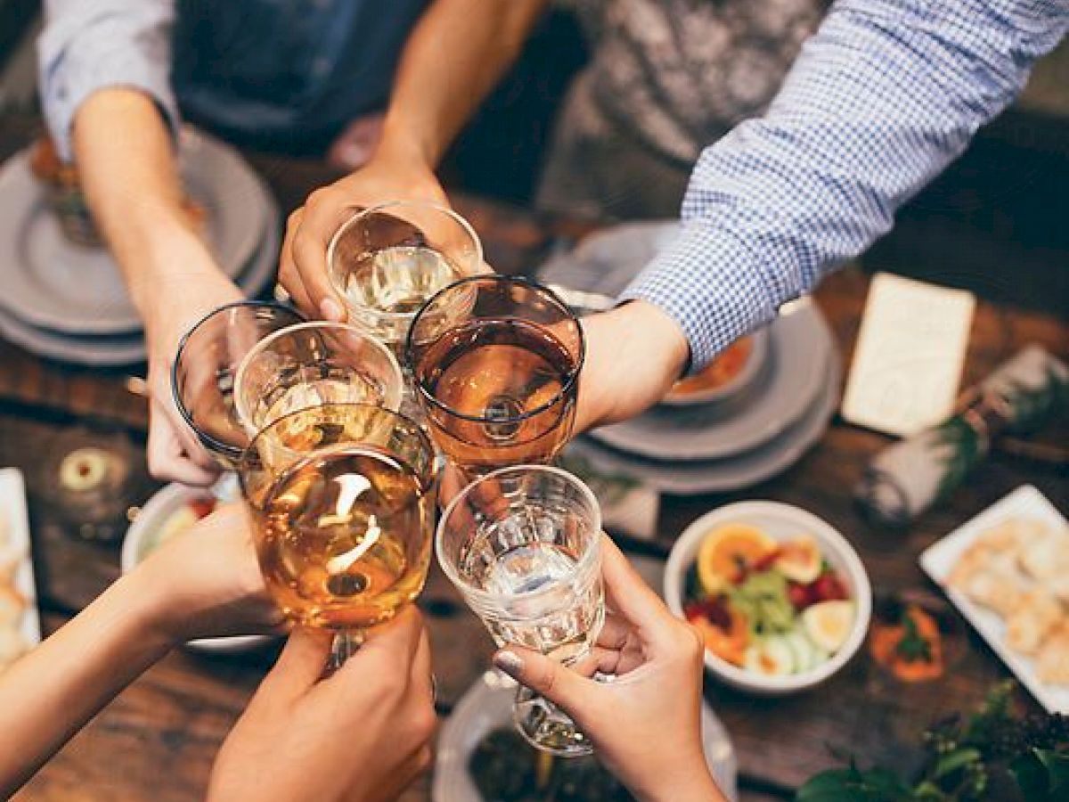 People are gathered around a table toasting with glasses, with plates of food in the background.